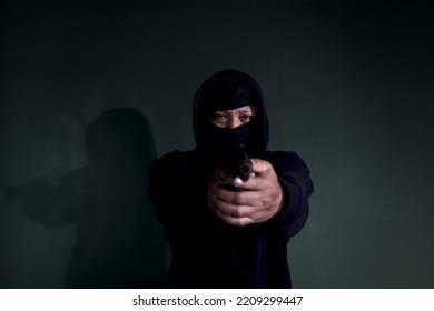 Criminal Man In Black Hood Holding A Gun Pointing Victim, Mask Thief Robber With His Gun On Hands To Commit Crime And Robbery.