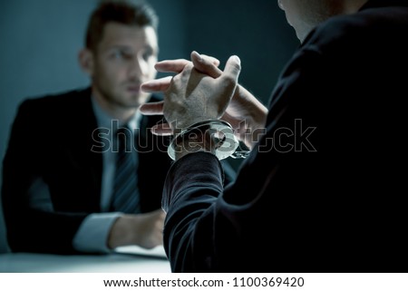 Criminal man with handcuffs being interviewed in interrogation room after committed a crime
