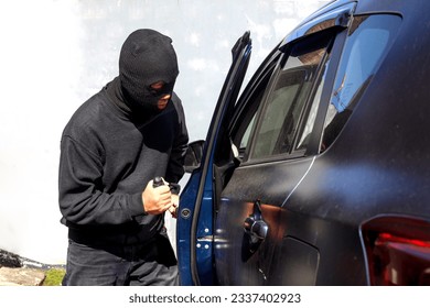 Un criminal con la puerta abierta y la entrada al auto. Él usa un destornillador. Hijacker, el concepto de robo de coches