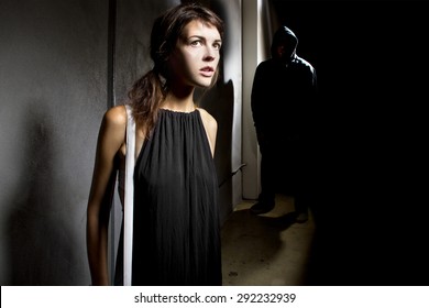 Criminal Stalking A Woman Alone In A Dark Street Alley.  He Is Hiding In The Shadows And The Woman Is Alone On The Street.