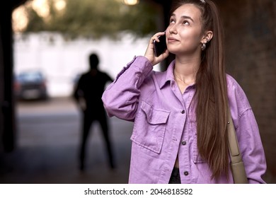 Criminal stalking woman, commiting a crime while victim was walking alone, talking on phone in dark street alley. Caucasian young woman is going to be raped by unrecognizable stranger