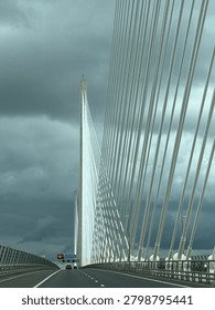 Cris cross patterns of white cables supporting bridge over Firth of Forth, Scotland set against dark grey sky.