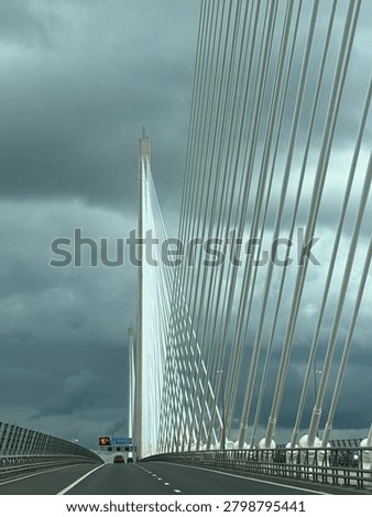 Cris cross patterns of white cables supporting bridge over Firth of Forth, Scotland set against dark grey sky.