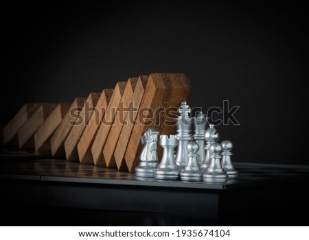 Crisis management, risk management, crisis solving or problem solving concept. Chess stopping wooden dominoes from collapsing on chessboard in black scene.