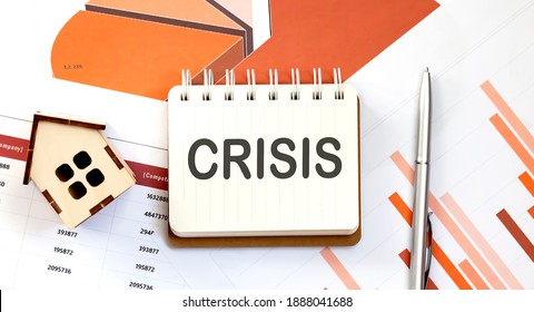 CRISIS text on notepad with paper sheet with pen and wooden house