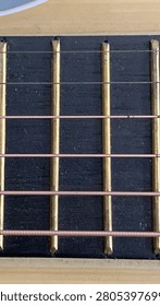 A crisp diagonal overhead macro image detailing the bridge system on a traditional western acoustic instrument face. The unique diagonal composition runs from the top-left to the bottom-right, showcasing the deep brown stained wooden bridge perfectly set against the natural bright wood background soundboard. Six bright white round pins line up precisely, anchoring the high-tension steel and bronze strings into the body structure just below the white plastic horizontal saddle piece. The clear view shows how the strings emerge and stretch upwards toward the neck and the long dark fretboard out of view. This artistic perspective captures the sleek geometry and curves of musical equipment, making it an excellent visual asset for instructional manuals, classical music publications, or commercial designs for a guitar manufacturer shop. It creates an engaging sense of movement across the surface, highlighting the intricate engineering required to hold proper tune and stable acoustic resonance across the whole bridge.