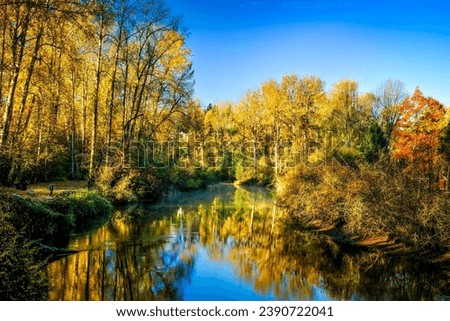 A crisp fall morning on the Sammamish River, with colorful trees and the blue sky reflected in the still water.