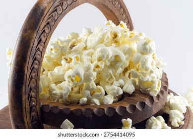 Crisp, fluffy popcorn overflows from a rustic hand-carved wooden bowl, isolated on a clean white background, perfect for various media.