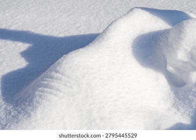 A crisp image showing the sharp edge of a snow drift with visible wind-sculpted patterns and a stark shadow.