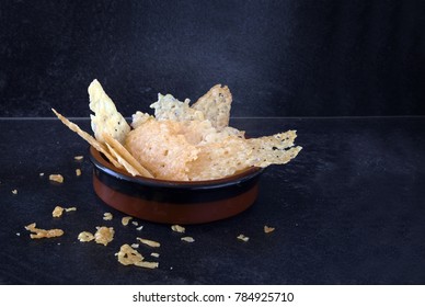 crisp parmesan cheese chips, homemade finger food snack in a bowl on a dark slate background with copy space, selected focus, narrow depth of field