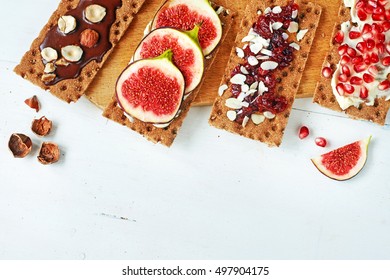 Crisp Rye Bread With Chocolate Paste And Hazelnut, Fig, Soft Cheese, Pomegranate, Cranberry Jam On A White Table. Copy Space.