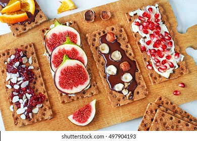 Crisp Rye Bread With Chocolate Paste And Hazelnut, Fig, Soft Cheese, Pomegranate, Cranberry Jam And Almond On A White Table. 