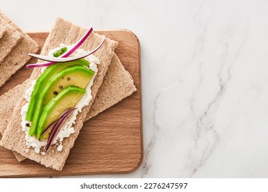 Crispbread with cream cheese and avocado on a wooden cutting board. Top view. Copy space.