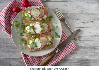 Crispbread sandwich with cottage cheese and sliced radish on a white plate on rustic wooden table background - Powered by Shutterstock