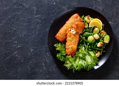 Crispy Beer Batter Cod Fish fillet with roast brussel sprouts, green beans, green peas and fresh lettuce on black plate on concrete table, horizontal view from above, flat lay, free space