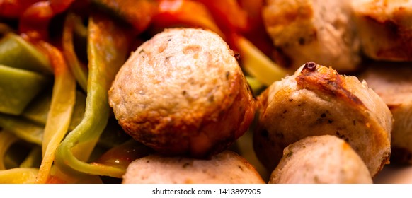 Crispy Bite-sized Pieces Of German Bratwurst With Green And Yellow Ribbon Noodles With Mashed Vegetables In Tomato Sauce