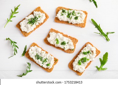 Crispy Bread Crackers With Cottage Cheese And Green Herb On White Background. Flat Lay.