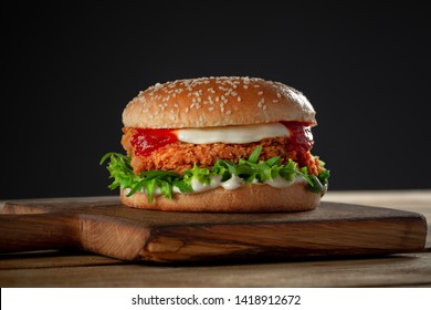 crispy, breaded chicken burger with mozzarella cheese standing on wooden cutting board