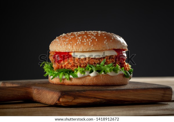 crispy, breaded chicken burger with\
mozzarella cheese standing on wooden cutting\
board