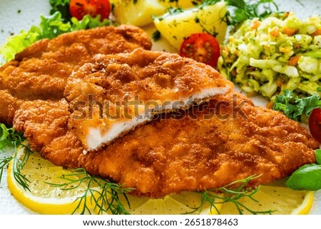Crispy breaded chicken cutlets with boiled potatoes and young cabbage salad on wooden table