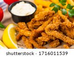 Crispy Breaded Clam Strips Snack Size. Deep Fried Breaded Clams Fingers and French Fried Potatoes with Tartar Dipping Sauce on a white wooden board. Selective focus.