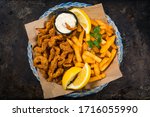 Crispy Breaded Clam Strips Snack Size. Deep Fried Breaded Clams Fingers and French Fried Potatoes with Tartar Sauce on Rustic Metal Background. Selective focus.