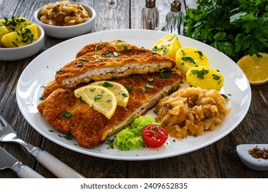Crispy breaded fried cutlet with boiled potatoes and cooked cabbage on wooden table 