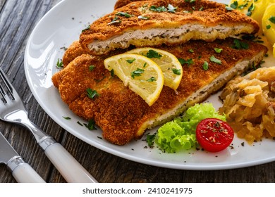 Crispy breaded fried cutlet with boiled potatoes and cooked cabbage on wooden table 