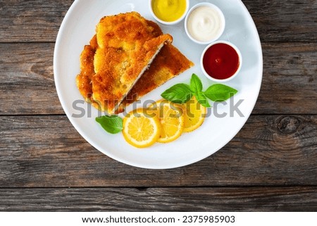 Crispy breaded seared chicken cutlet with lemon slices and fresh vegetables on wooden table 