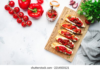 Crispy bruschetta with soft goat cheese and sweet red paprika in olive oil with herbs served on cutting board on white kitchen table background, top view - Powered by Shutterstock