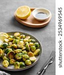 Crispy brussels sprouts in a plate with soy or balsamic sauce and sesame on a dark  background with fork and lemon. Concept of a healthy vegetable vegetarian dish in rustic style.