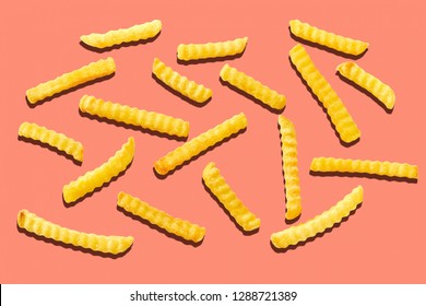 Crispy crinkle cut potato chips, pommes frites or French fries scattered randomly on an orange background in a flat lay overhead view