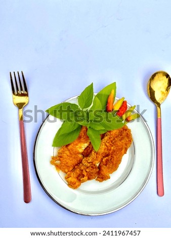 Crispy deep fried chicken breast on the white plate garnished with fresh basil leafs and colorful chilly served using fox and spoon
