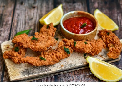
 Crispy  deep fried   chicken strips and wedges potato. Breaded  with cornflakes chicken  breast fillets  with chilly peppers and fresh   basil on wooden rustic background