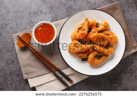 Crispy delicious fried shrimp with salted egg yolks, curry leaves and chili peppers served with chili sauce close-up in a plate on the table. Horizontal top view from above
