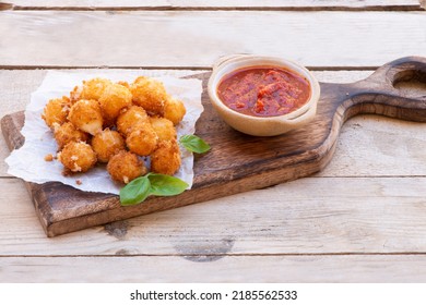 Crispy Dip Fried Baby Mozzarella Served With Spicy Tomato And Garlic Sauce And Basil Leaves On A Wooden Cutting Board