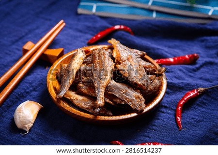 Crispy dried small fish on flower plate with dark purple cloth