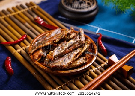 Crispy dried small fish on flower plate with dark purple cloth