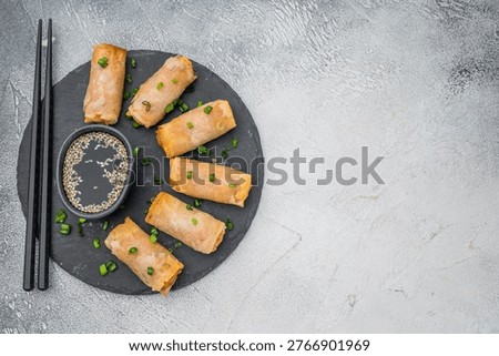 Crispy Egg rolls arranged on round slate plate with soy sauce and sesame seeds flat lay light background.