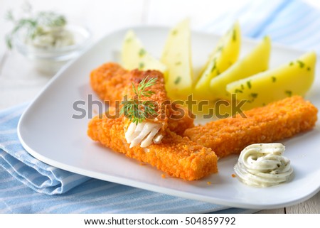 Crispy fish fingers of breaded pollack fillet served with parsley potatoes and remoulade sauce on a white plate