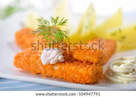 Crispy fish fingers of breaded pollack fillet served with parsley potatoes and remoulade sauce on a white plate - selective focus