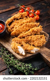Crispy fried Breaded chicken strips, breast fillet meat with tomato ketchup on a plate. Wooden backgrund. Top view.