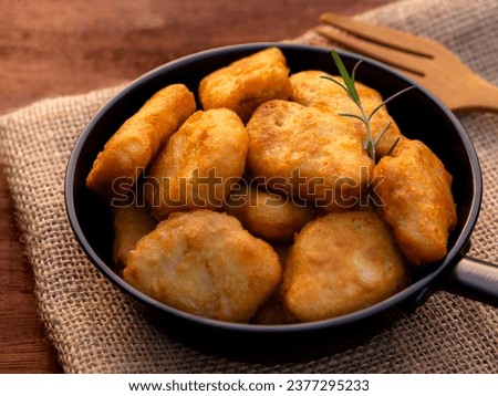Crispy fried chicken nuggets and rosemary in mini pan on wooden table background.