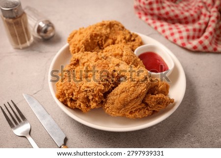 Crispy fried chicken served on a plate with ketchup, fork, knife, and pepper shaker.
