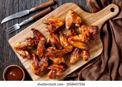 crispy fried chicken wings served on a wooden board with barbeque sauce on dark wooden table, flat lay