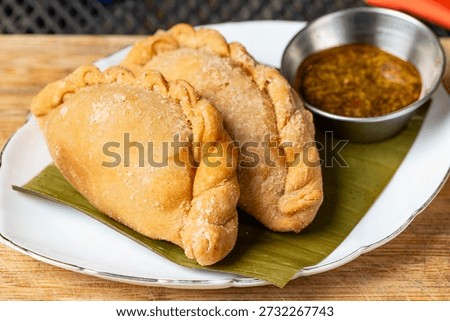 Crispy fried empanadas serving on a white plate with chimichurri dipping sauce