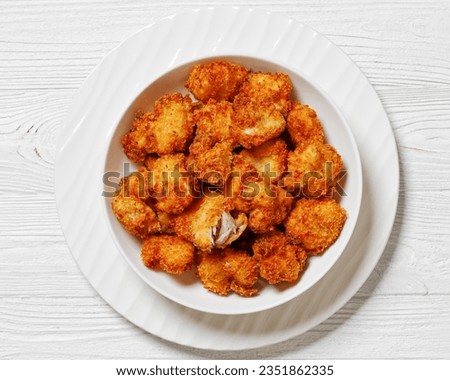 crispy fried panko breaded chicken bites in white bowl on white wooden table, horizontal view from above, flat lay, close-up