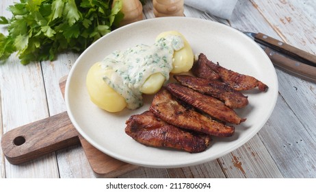Crispy fried pork with creamy parsley sauce and boiled potato in the plate on the table or stegt flæsk, a classic Danish cuisine. - Shutterstock ID 2117806094