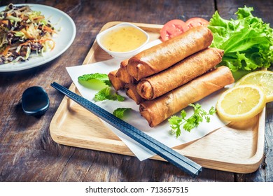 Crispy fried spring rolls with plum sauce and salad, lemon slices on wooden table