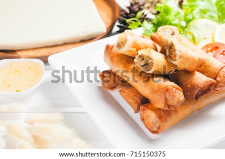 Crispy fried spring rolls with plum sauce and salad, lemon slices on wooden table
